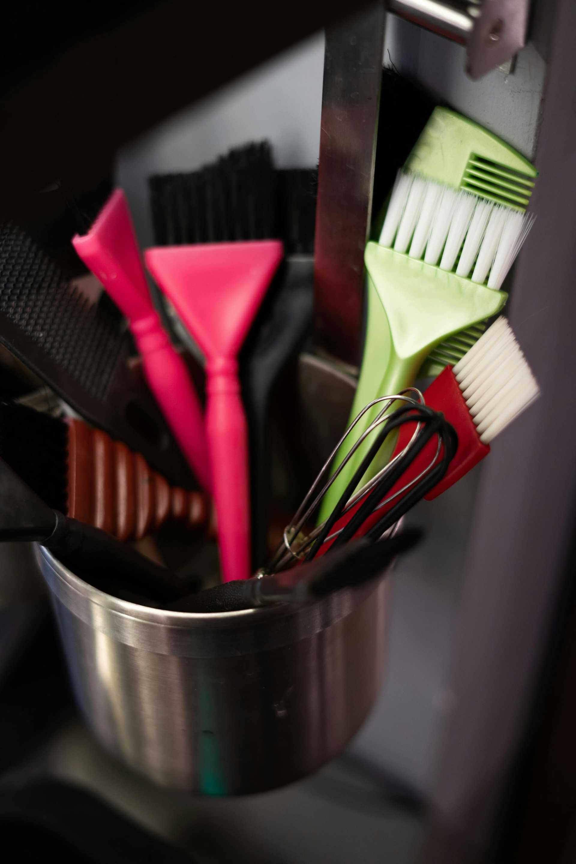 Kitchen utensils in a metal container, including brushes and whisks.